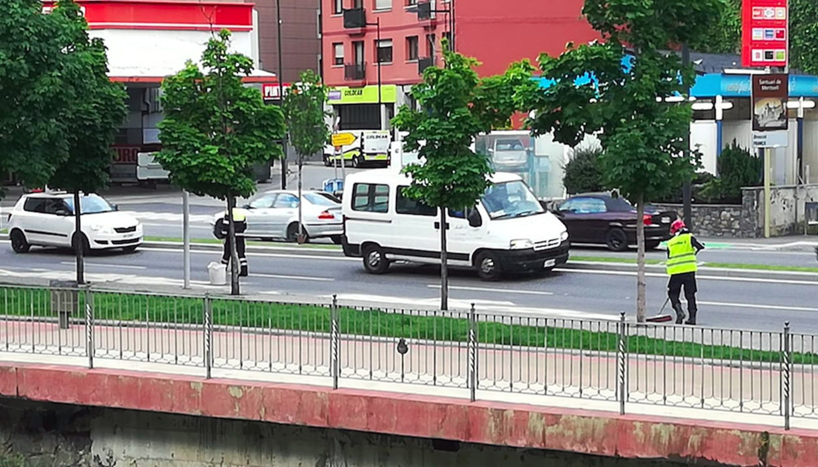 Un agent dels bombers neteja la calçada alhora que un agent de circulació supervisa el trànsit.