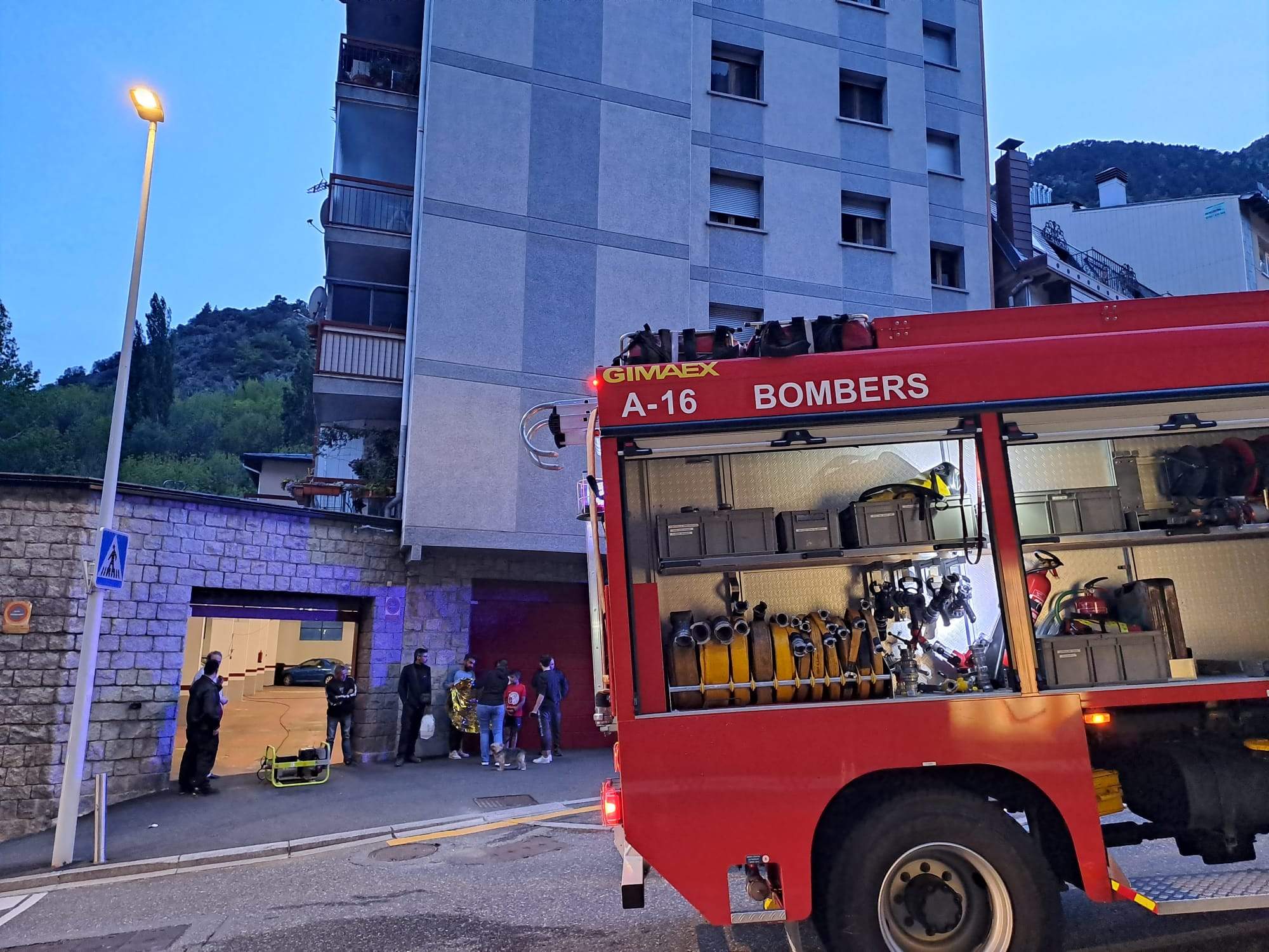 Un camió dels bombers estacionat en el lloc de l'incendi amb veïns desallotjats fora al carrer.
