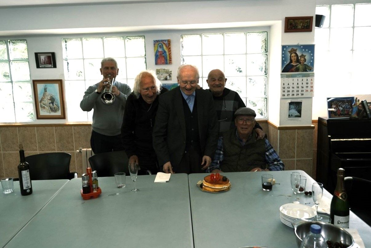 Els quatre mossens amb el pastís d'aniversari i amb mossèn Grau tocant la trompeta. Els quatre mossens amb el pastís d'aniversari i amb mossèn Grau tocant la trompeta.