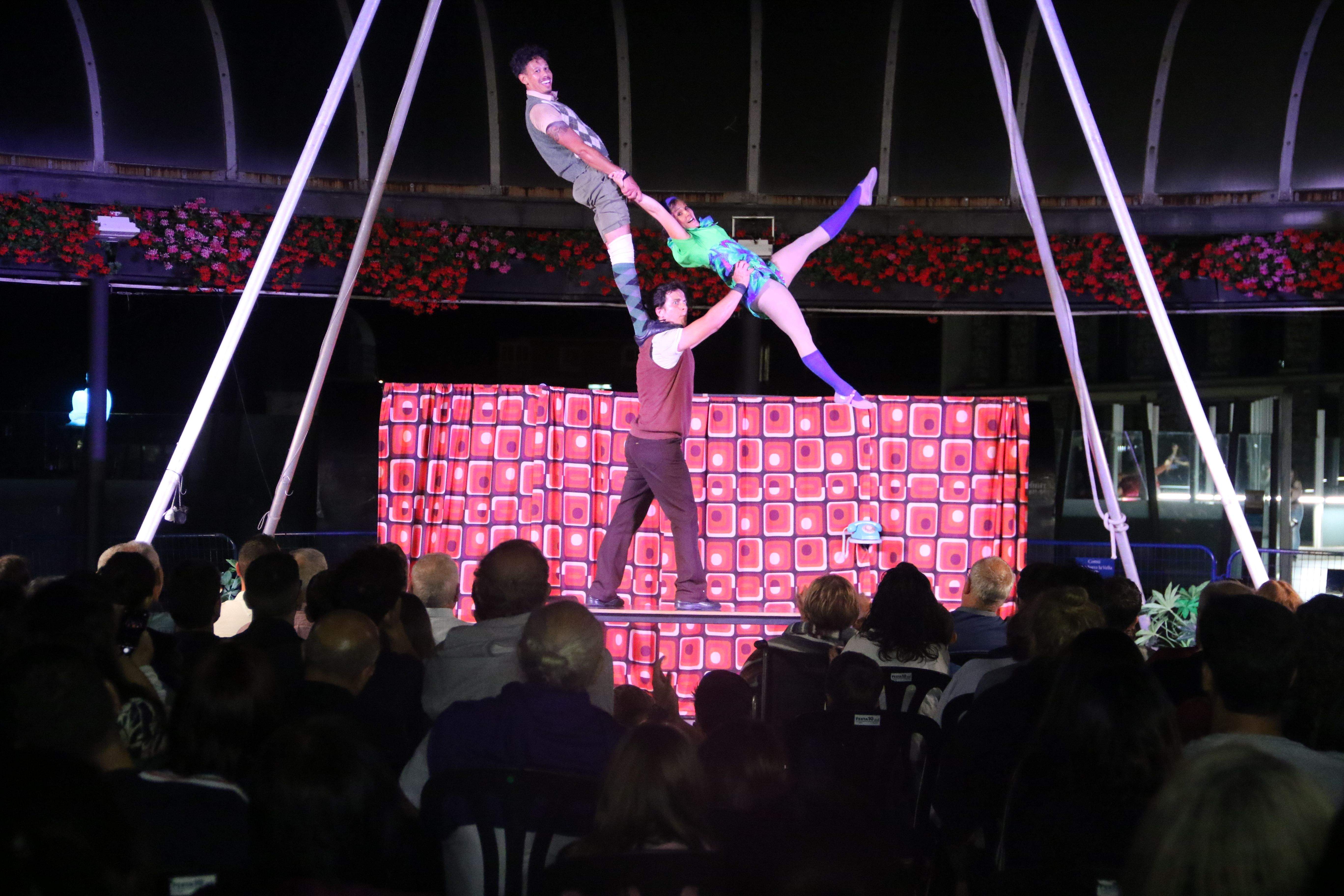 Els tres acròbates de la Cía. Circo Los en plena acció, amb totes les cadires previstes a la plaça del Poble plenes de gom a gom.