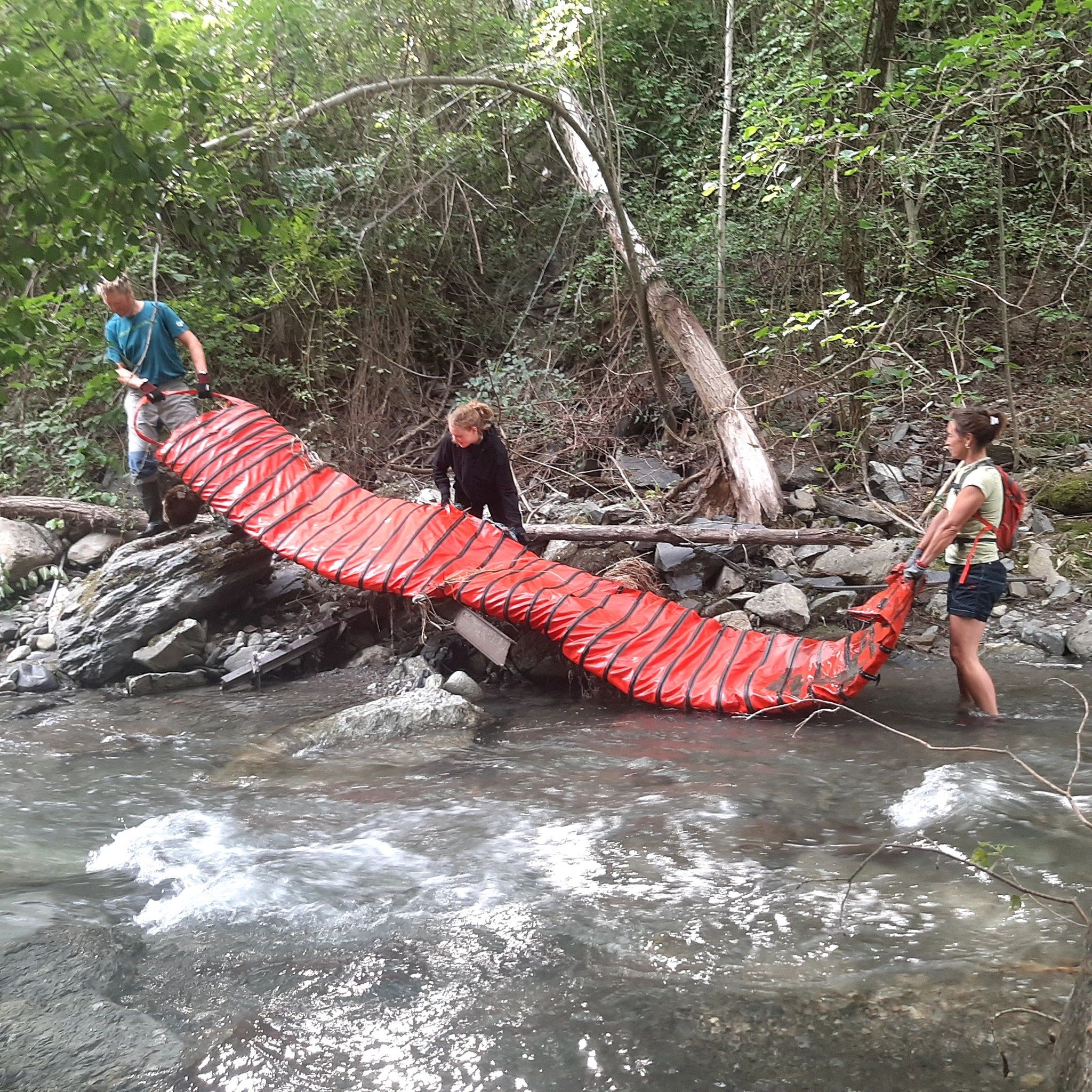 Tres voluntaris treuen una gran lona vermella del riu.