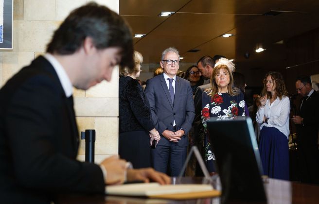 Ensenyat signant el llibre, amb ministres i altres autoritats esperan.