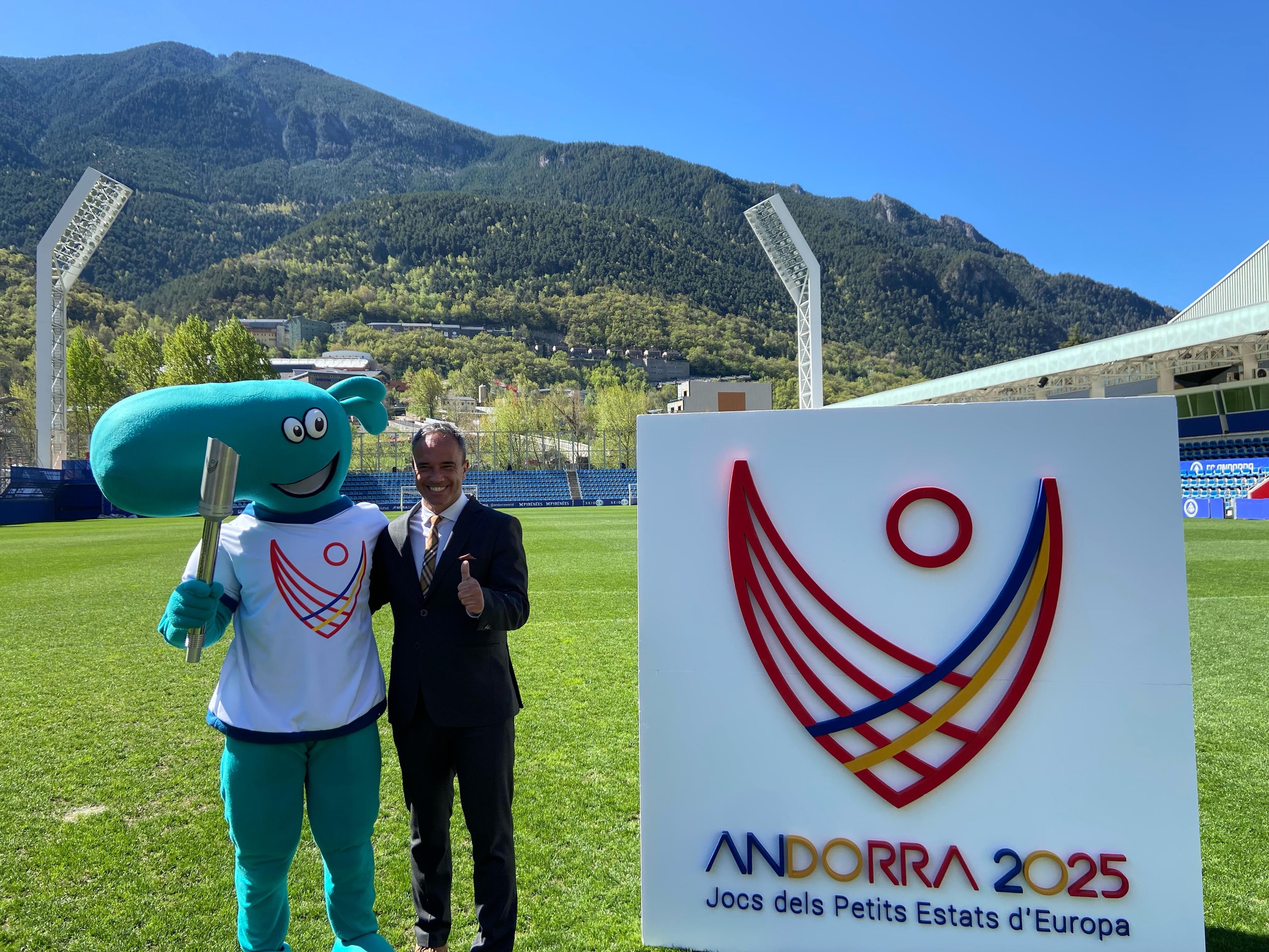 El secretari d'Estat, Alain Cabanes, amb la mascota, la torxa i el logotip d'Andorra 2025.