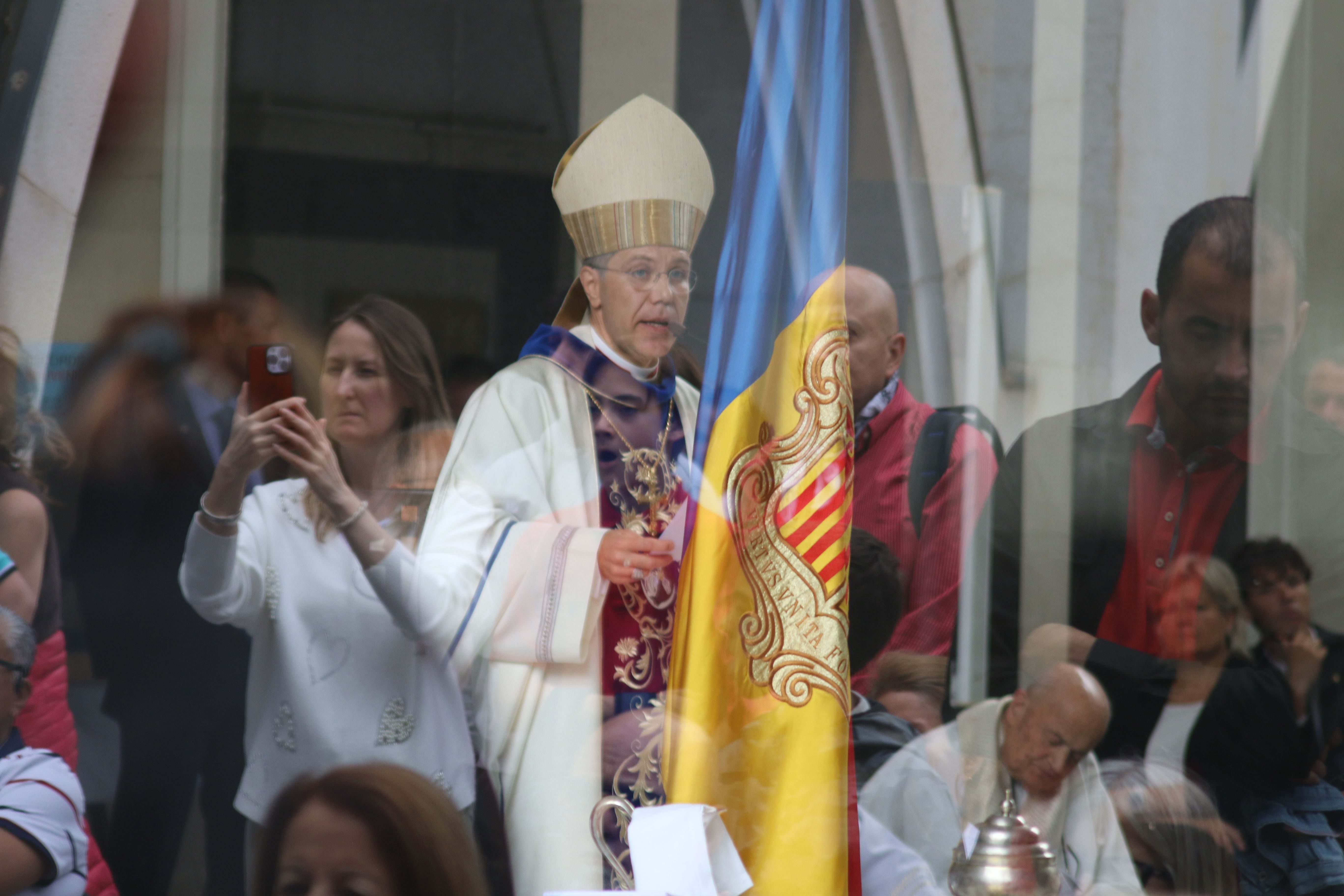 El bisbe Copríncep, Josep-Lluís Serrano, durant l'homilia, amb tot d'assistents a la missa escoltant-lo dins l'església o reflectits a la vidriera.