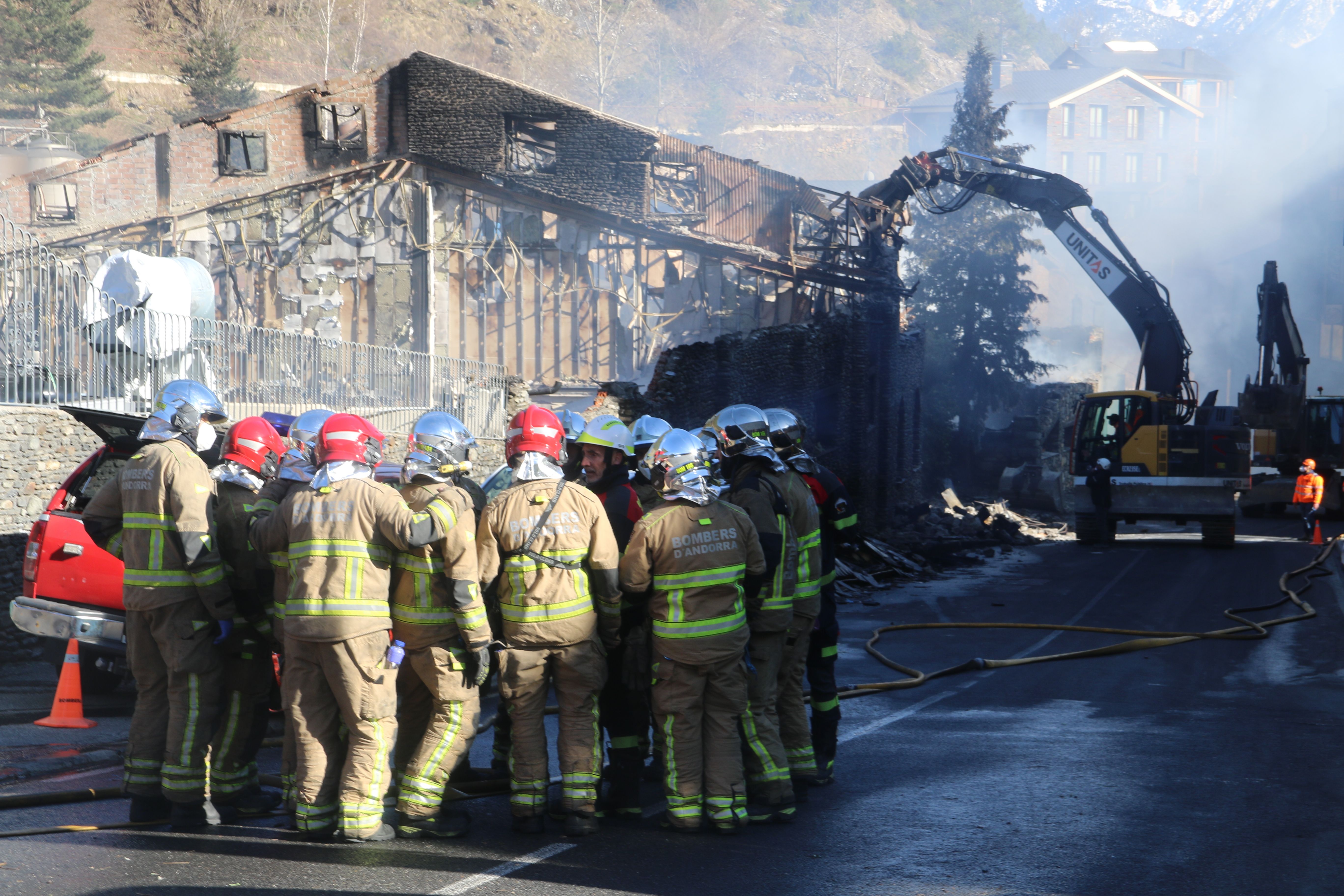 Bombers fent una trobada de coordinació mentre la màquina tomba parts de l'estructura de la fàbrica. Bombers fent una trobada de coordinació mentre la màquina tomba parts de l'estructura de la fàbrica.