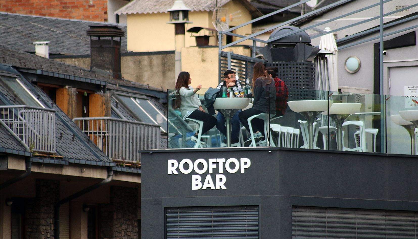 Quatre persones fent petar la xerrada i la beguda en una terrassa exterior d'un bar al capdamunt d'un edifici al centre d'Andorra la Vella.