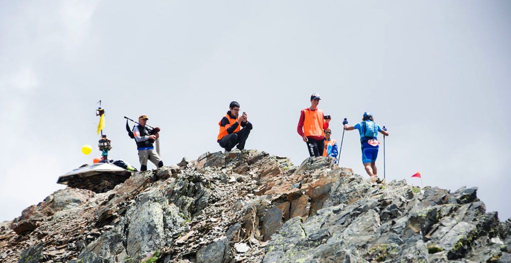 Un corredor arriba a un cim de l'Ultra Trail entre voluntaris en una edició anterior.