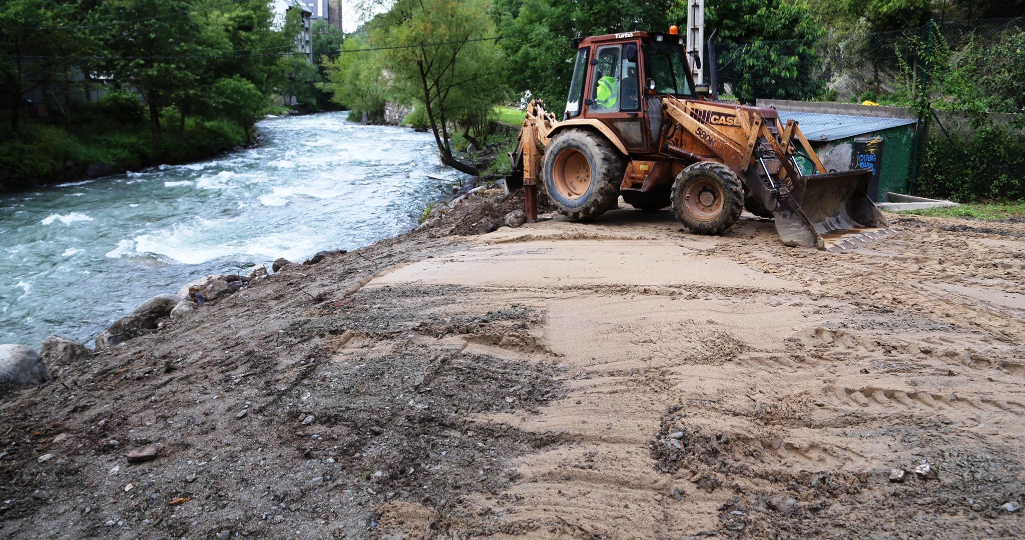 Una excavadora treballa en la col·locació de la sorra a la platja fluvial.