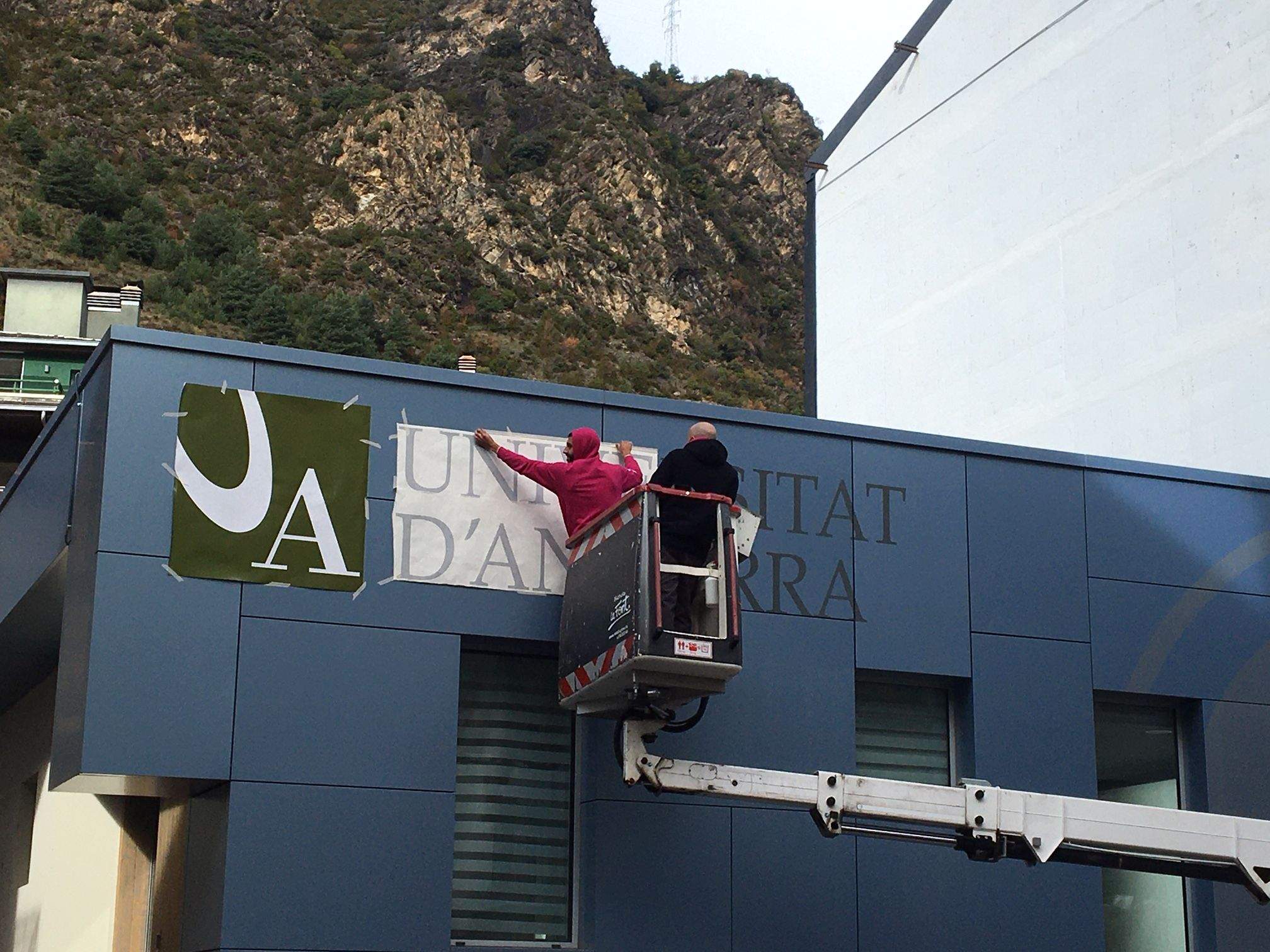 Uns operaris col·loquen el nom de la universitat a la façana del local.