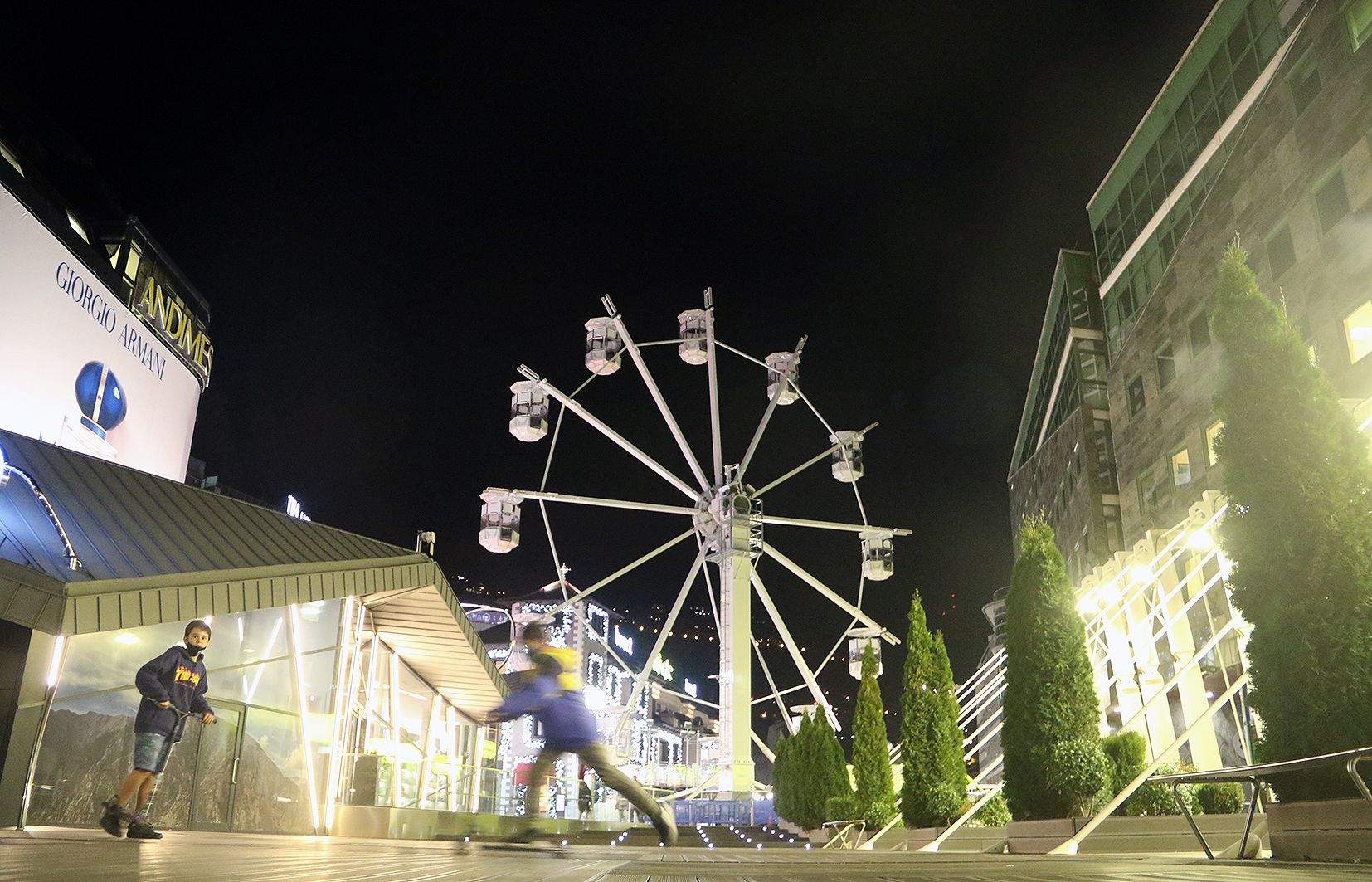 Dos adolescents patinant a la zona de la Rotonda amb la nòria ja muntada al fons.