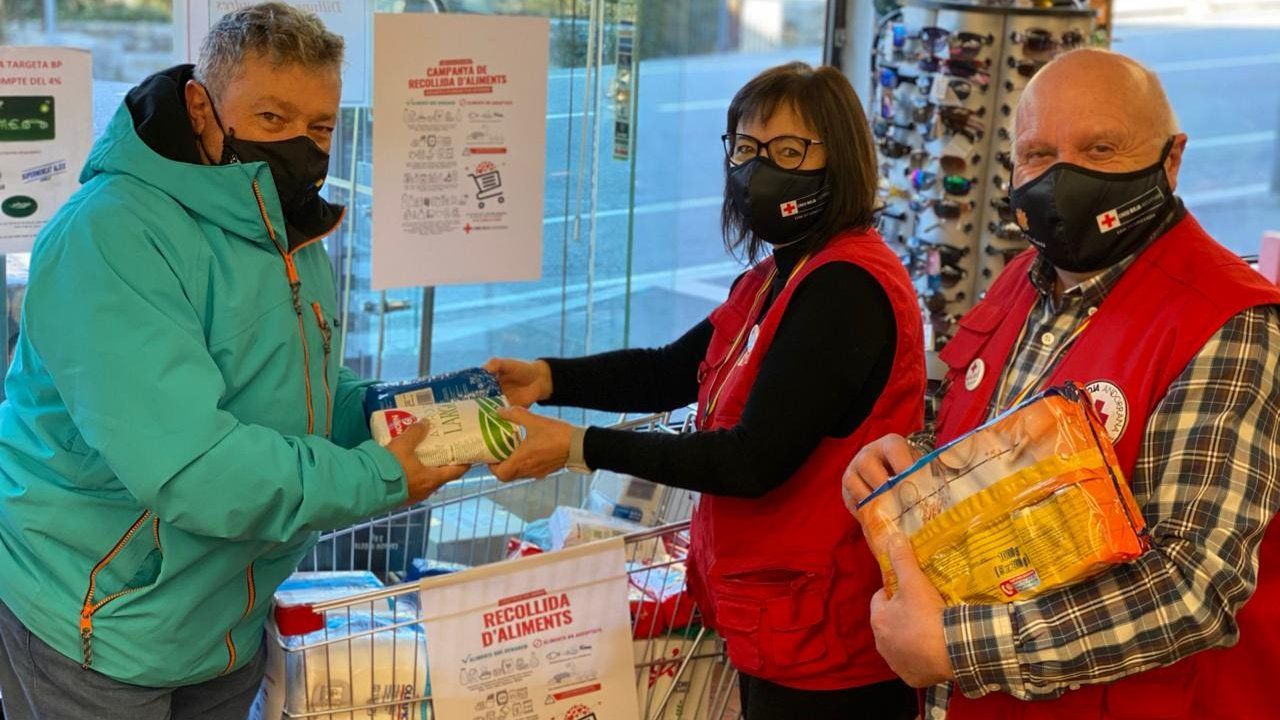 Voluntaris de Creu Roja agafen productes que els entrega un home.