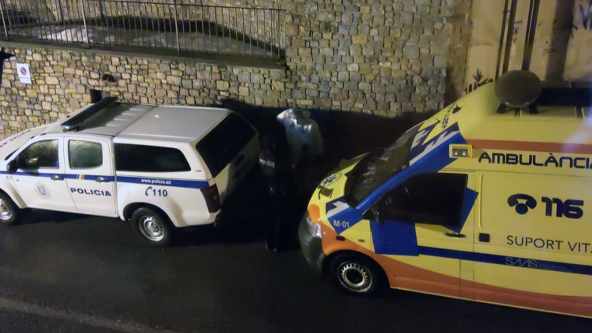 Un sanitari i un agent entre un vehicle policial i l'ambulància al peu de l'immoble on han passat els fets.