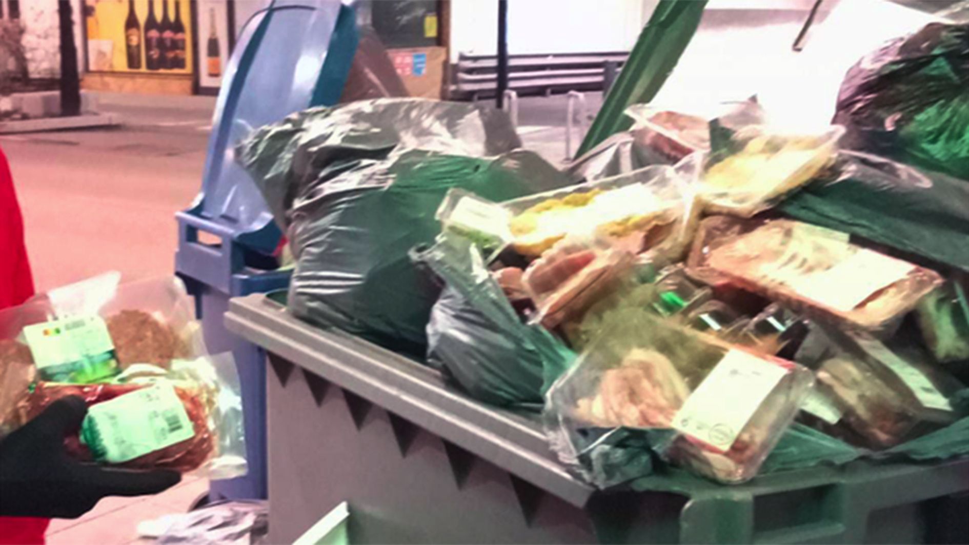 Dos ciutadans agafant envasos d'hamburgueses d'un contenidor.