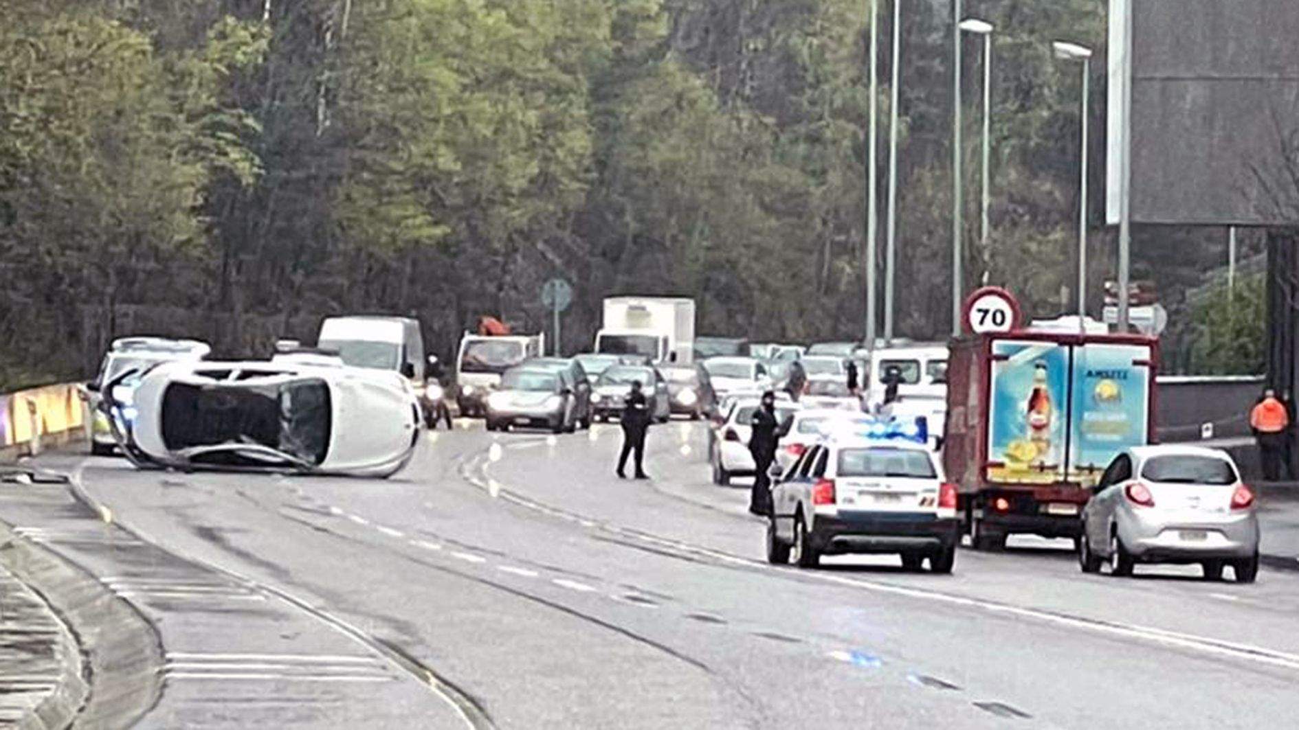 La policia regulant el trànsit amb el cotxe bolcat a l'esquerra.