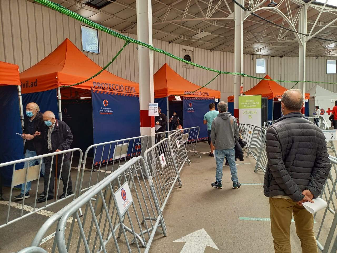 Persones fent cua esperan torn per vacunar-se mentre un home es dirigeix a la zona d'espera.