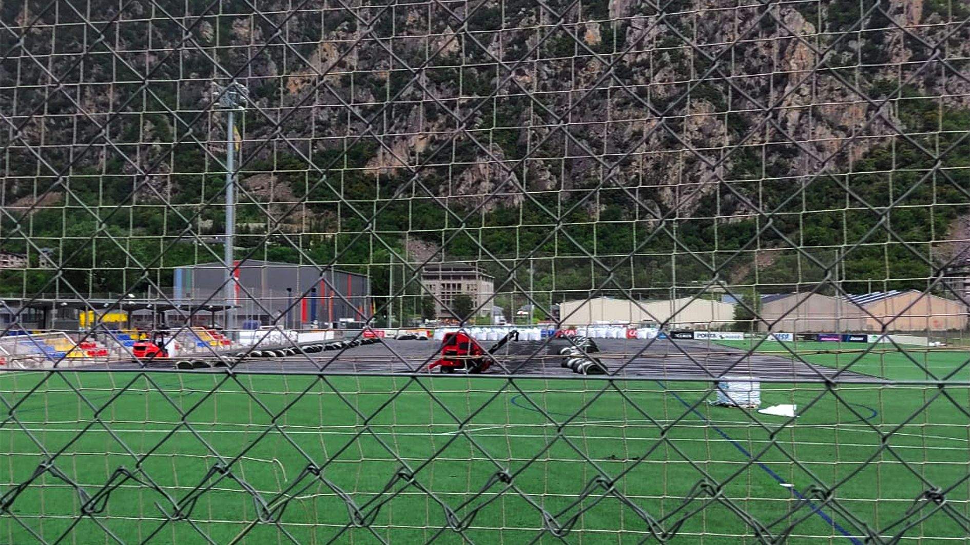 Les màquines retirant la gespa d'un dels camps de la Margineda vistos a través del reixat que protegeix el recinte.