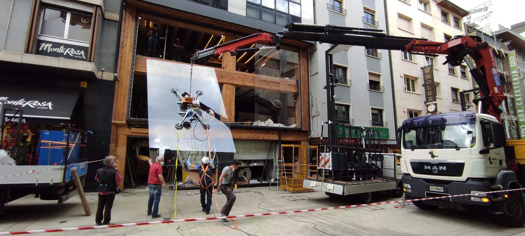 El braç articulat maniobrant amb el vidre suportat per les ventoses ajudades per diferents operaris.