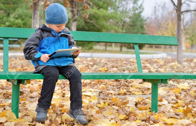 23184341 niño leyendo un equipo tablet pc mientras está sentado solo en un banco de madera en el parque en ot
