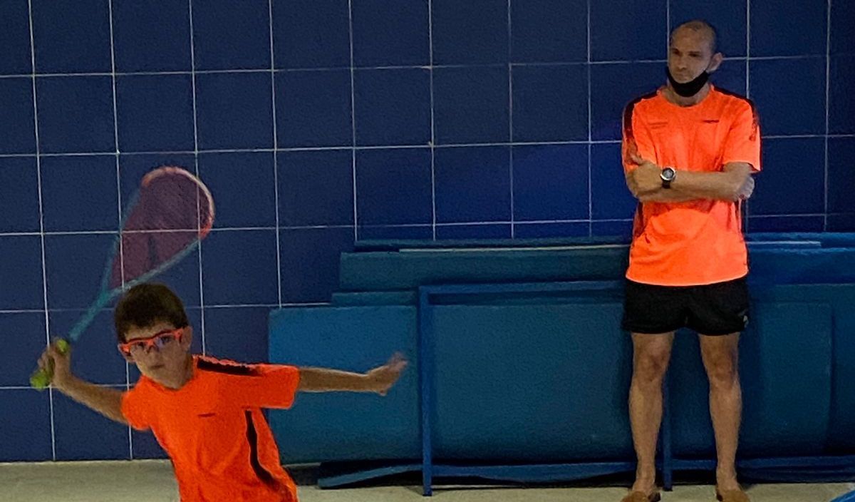 L'Izan es disposa a colpejar una bola sota l'atenta mirada del seu entrenador.